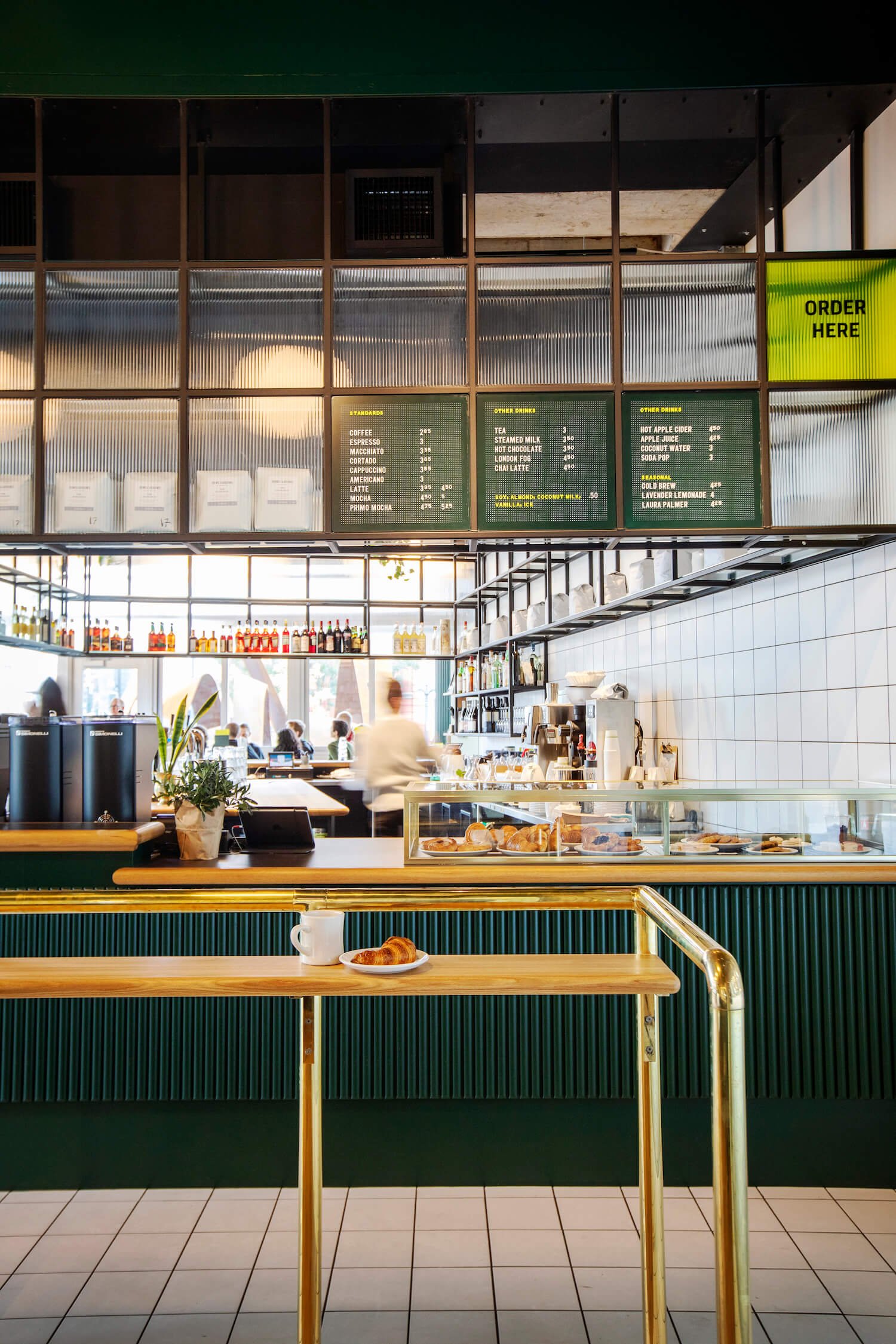 A full view of the Sherwood coffee bar counter. In front of it sits a croissant and cup of coffee with people working behind the counter